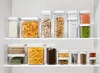 A collection of clear plastic food storage containers with white lids, neatly arranged on white shelves. Náhľad obrázku produktu