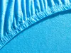 A close-up view of a turquoise jersey fitted sheet, showing the elasticized edge and the texture of the fabric. Produktbild-Vorschau