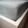 A close-up view of a grey fitted sheet on a white bed frame. Náhled obrázku produktu