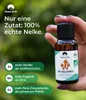 A hand holding a small bottle of essential oil with text overlays highlighting its benefits. Produktbild-Vorschau