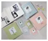 A collection of pastel-colored photo albums and smaller photo frames arranged on a light-colored wooden surface, with a few small decorative flowers scattered around. Voir les images du produit