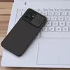 A black phone case with a camera cover is placed on a white laptop keyboard. Náhled obrázku produktu
