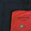A close-up view of a red blanket folded over a black fabric, with text and a logo overlayed on the red section. Anteprima dell’immagine prodotto