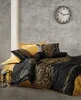A bed with black and gold patterned bedding and yellow pillows against a textured gray wall with a clock. Produktbild-Vorschau