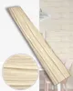 A wooden plank with a wood grain texture is shown diagonally across a white background, with a close-up inset of the texture in the lower left. The background also shows a hint of a room with a light fixture and a pink chair. Anteprima dell’immagine prodotto