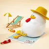 A cute duck toy wearing a hat, relaxing on a beach towel with drinks and a deck chair. Produktbild-Vorschau