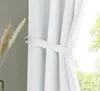 A close-up of a white curtain tied back with a fabric band, with dried grass in the background. Produktbild-Vorschau