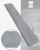 A long, thin gray tile with a textured surface is shown diagonally across the image. A circular inset on the left shows a close-up of the tile's texture. The background features a blurred interior scene with stacked items and a bottle, along with a logo at Produktbild-Vorschau