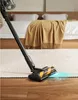 A person is vacuuming a carpeted floor in a bedroom setting with a bed and a blanket visible in the background. Náhled obrázku produktu