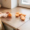 A person is cutting an orange on a transparent cutting board on a kitchen counter. Produktbild-Vorschau
