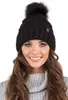 A woman wearing a black knitted beanie with a pom-pom and a grey sweater. Náhled obrázku produktu