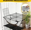 A multi-level cat cage with a hammock and a plant in the background. Náhľad obrázku produktu