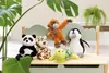 A collection of stuffed animals, including a turtle, panda, leopard, monkey, and penguin, are arranged on a light green shelf with a wooden frame. Large green leaves from a plant are in the foreground and background, suggesting a natural or playful environ Produktbild-Vorschau