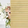 A bouquet of flowers in a glass vase, partially obscured by a beige pleated blind. Produktbild-Vorschau