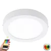 A white, circular LED ceiling light is shown against a white background. A hand is holding a smartphone displaying a color selection interface, suggesting smart control of the light. Náhľad obrázku produktu