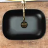 A top-down view of a black oval basin sink with a gold faucet, placed on a wooden surface. Náhľad obrázku produktu