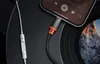 A close-up shot of a USB-C to Lightning adapter plugged into a smartphone, with a white headphone cable and a vinyl record in the background. Podgląd zdjęcia produktu