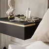 A close-up of a black floating nightstand with gold trim, decorated with a bust, pearls, and beauty products. Produktbild-Vorschau
