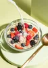 A bowl of oatmeal with berries and milk being poured into it, with a spoon to the side. Produktbild-Vorschau