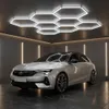 A white car is parked in a modern garage with hexagonal ceiling lights and vertical strip lights on the walls. Podgląd zdjęcia produktu