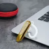 A gold wireless earbud with a white ear hook rests on a silver laptop keyboard. A black and red carrying case is visible in the background. Produktbild-Vorschau
