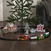 A Christmas train set is set up around the base of a Christmas tree on a wooden floor. Podgląd zdjęcia produktu