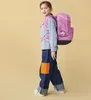 A young girl wearing a backpack and jeans, posing against a plain background. Voir les images du produit