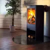 A modern fireplace with a glass base and a potted plant next to it, set against a wood-paneled wall. Produktbild-Vorschau