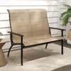 A tan and black outdoor bench sits on a patio with a white wooden wall in the background. Anteprima dell’immagine prodotto