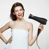 A woman wrapped in a towel holds a black hairdryer. Produktbild-Vorschau
