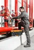 A man in work clothes is adjusting a valve on a large red pipe system, with a toolbox placed on a ledge nearby. Produktbild-Vorschau