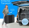 A woman is loading a large storage bag into the back of a car. The car's trunk is open, and the bag is being placed inside. The scene suggests easy transport of the item. Produktbild-Vorschau