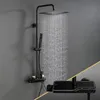 A black shower system with a square overhead showerhead and a handheld showerhead, mounted on a gray wall. Water is actively flowing from the overhead showerhead. Anteprima dell’immagine prodotto