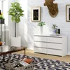 A modern living room scene featuring a white dresser with six drawers, a large potted plant, and decorative items. Produktbild-Vorschau