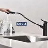 A hand is using a black kitchen faucet with a pull-out sprayer to fill a glass pitcher with water. Produktbild-Vorschau