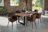 A dining table with chairs in a rustic industrial setting with exposed brick walls and large windows. Produktbild-Vorschau