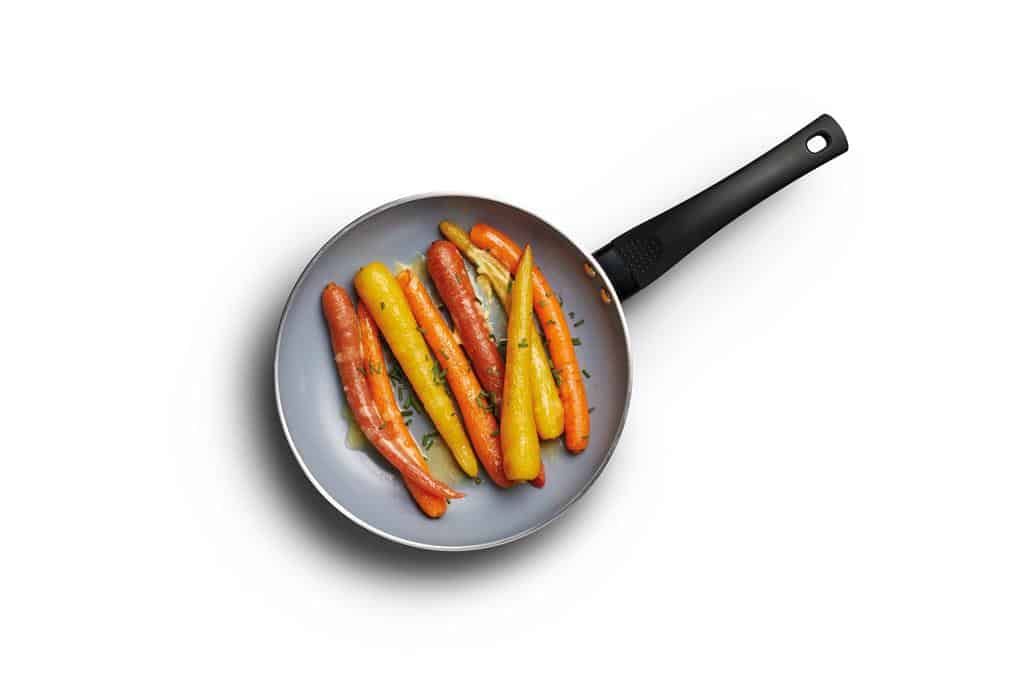 A frying pan with carrots inside, presented on a white background.