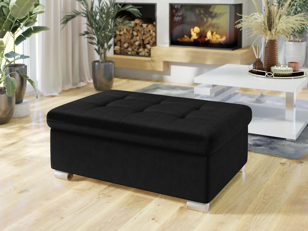 A black ottoman is placed in a living room setting with a fireplace and a coffee table.