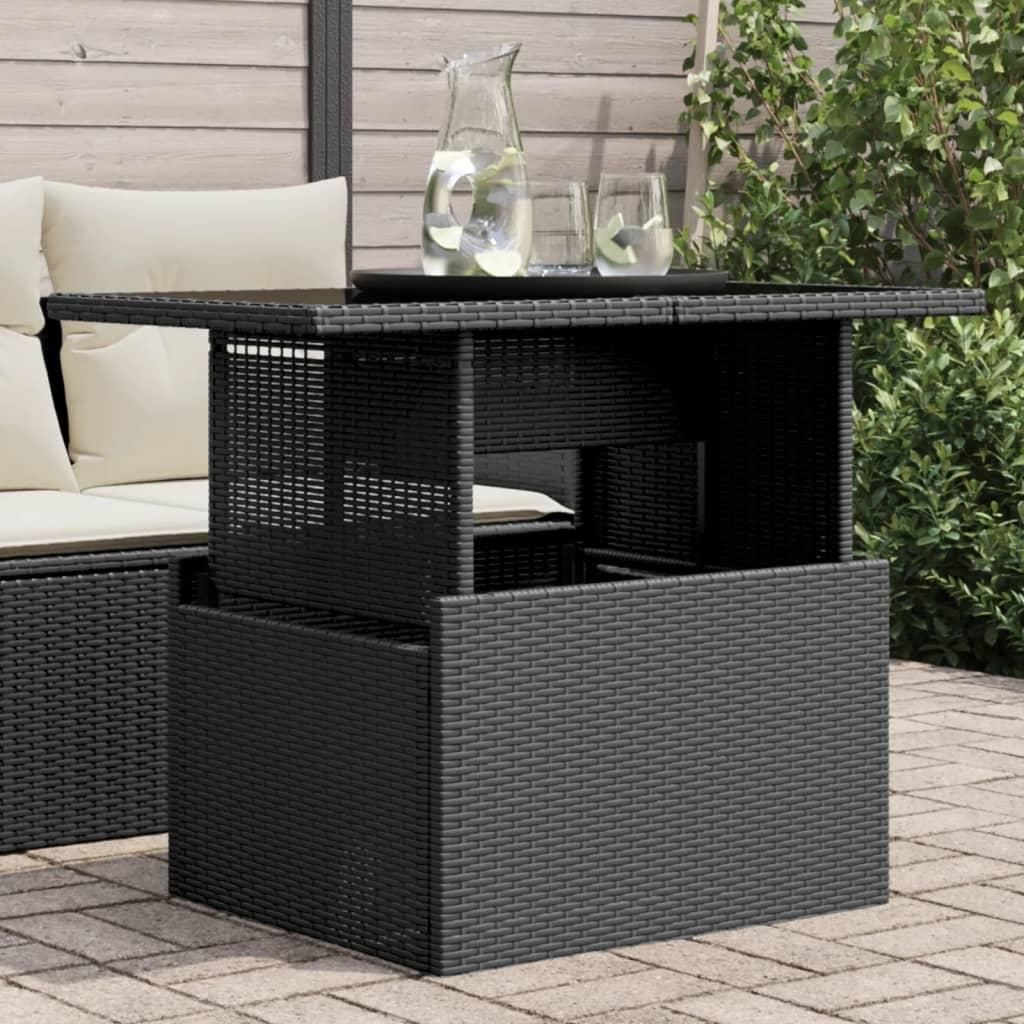 A black poly rattan garden table with a glass top is shown outdoors on a patio, next to a sofa with cushions. There are two glasses and a jug of water on the table.