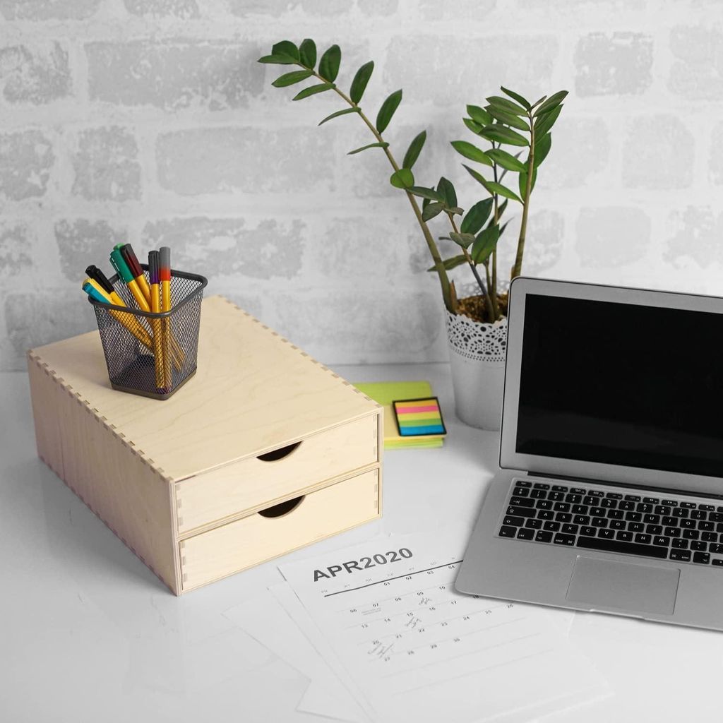 A wooden desk organizer with drawers, a pen holder with pens, a laptop, a potted plant, and a calendar page on a white desk.