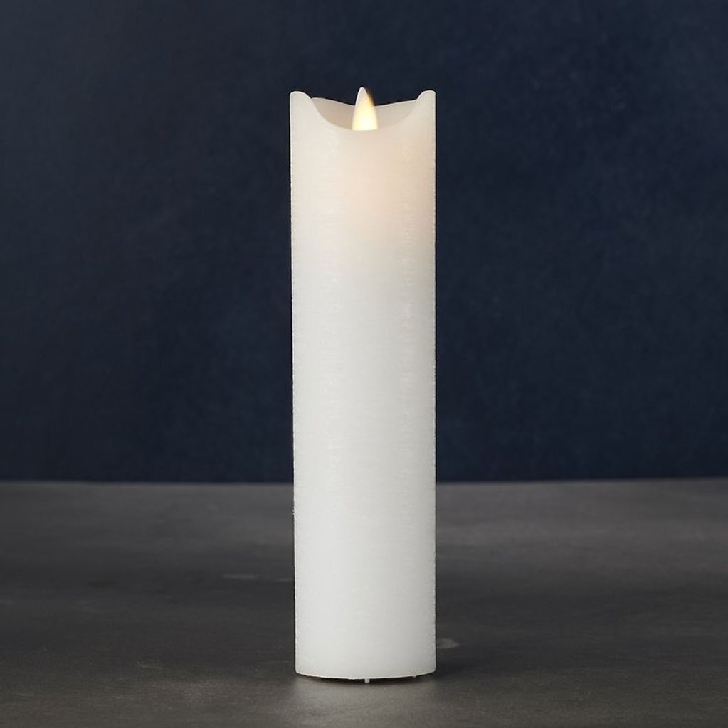 A white LED candle with a flickering flame sits on a dark surface against a dark blue background.