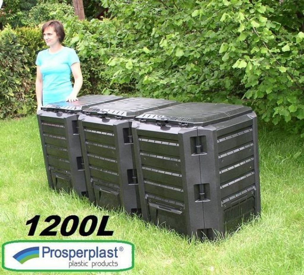 A woman stands next to three black compost bins in a grassy yard with trees in the background.