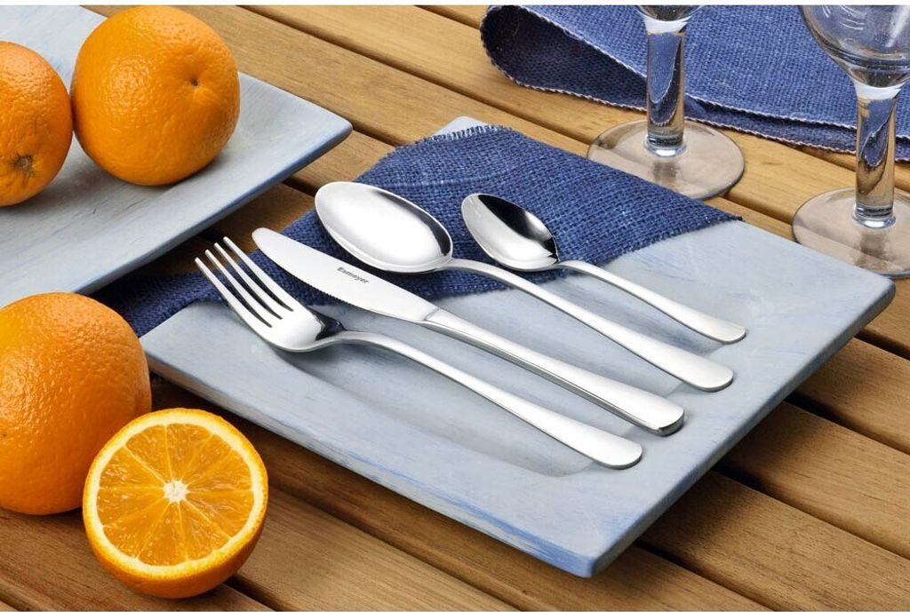 Cutlery set on a plate with oranges on a wooden table.