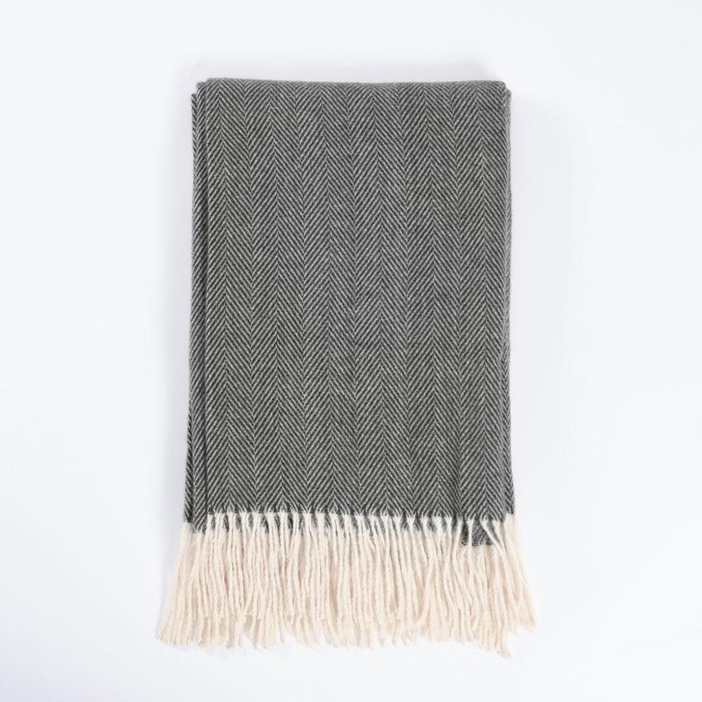 A folded gray herringbone blanket with cream fringe is laid flat on a white background.