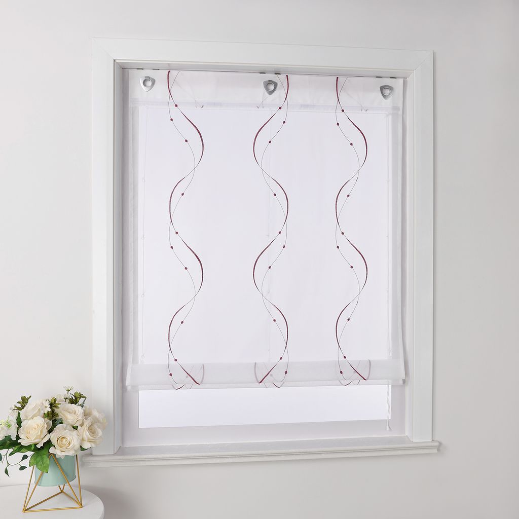 A white sheer roller blind with embroidered purple wavy lines and dots is shown hanging in a window frame. A small bouquet of white flowers in a teal pot sits on a surface to the left.