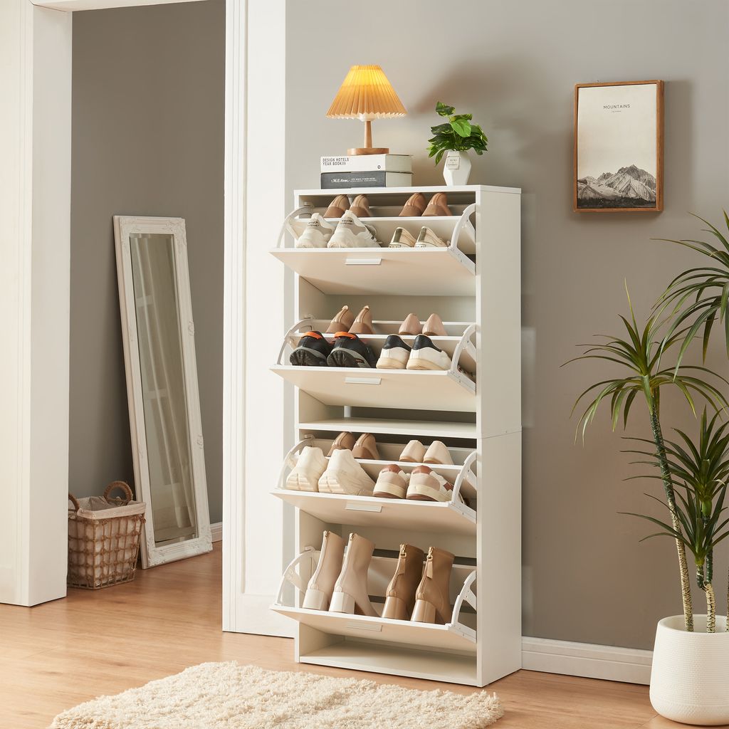 A white shoe cabinet with multiple flip-out drawers filled with shoes, placed in a hallway next to a mirror and a plant.