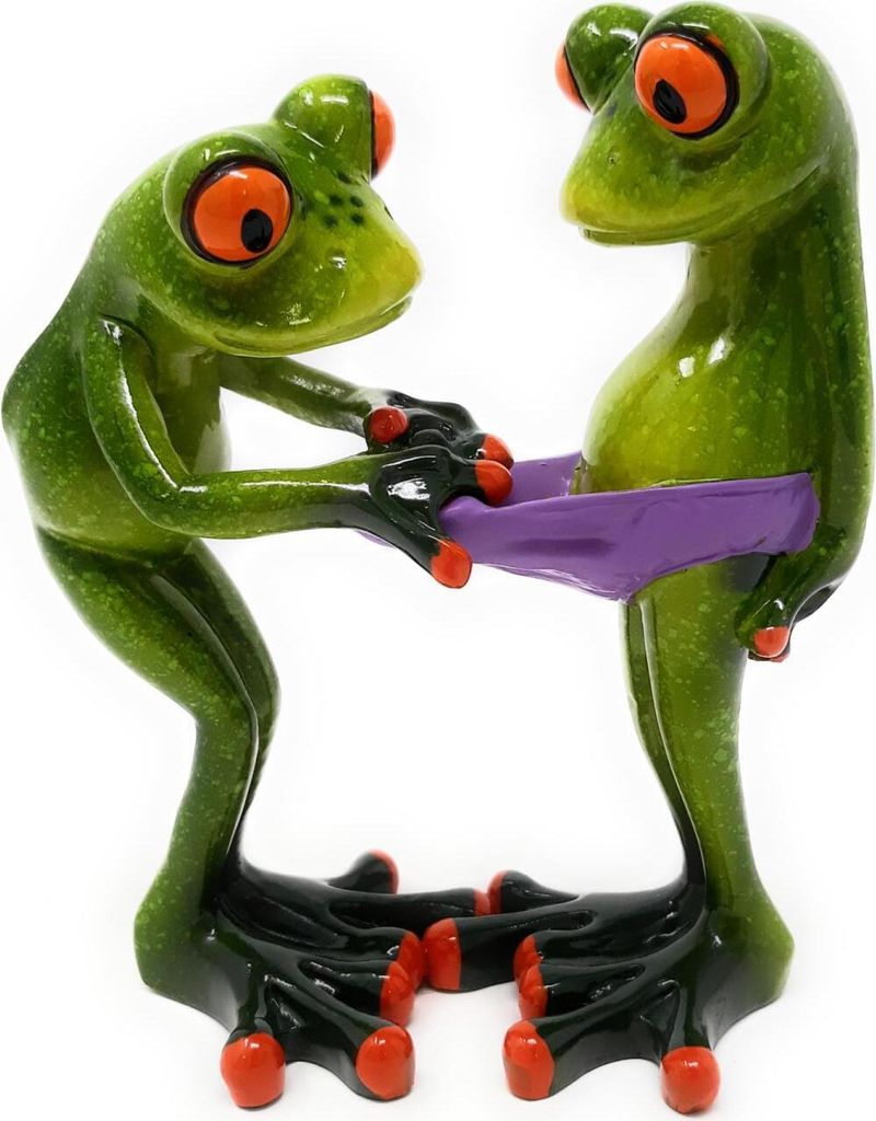 Two green frog figurines with large orange eyes are standing and holding a purple object between them.