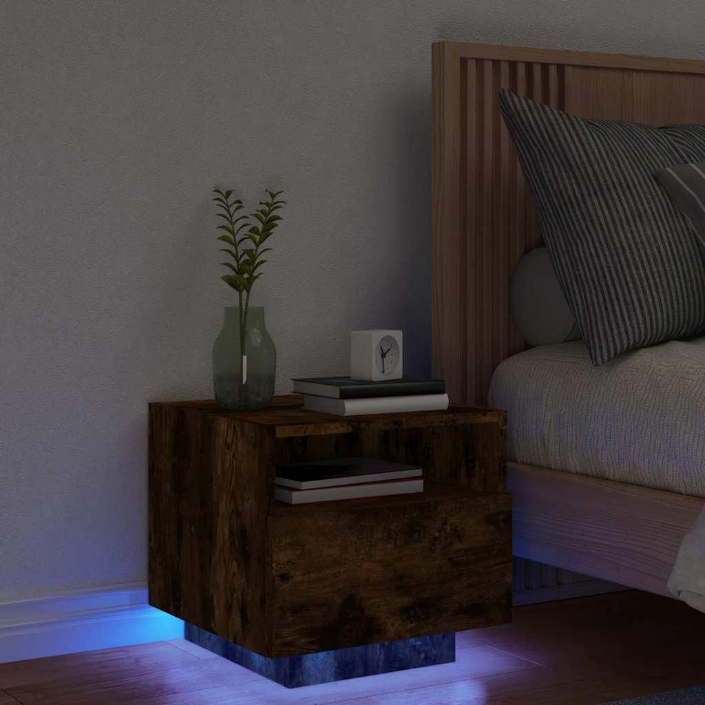 A bedside table with a vase of plants and books, next to a bed.