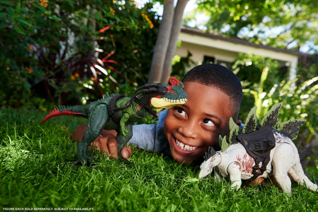 A young boy is playing with dinosaur toys in the grass in front of a house.