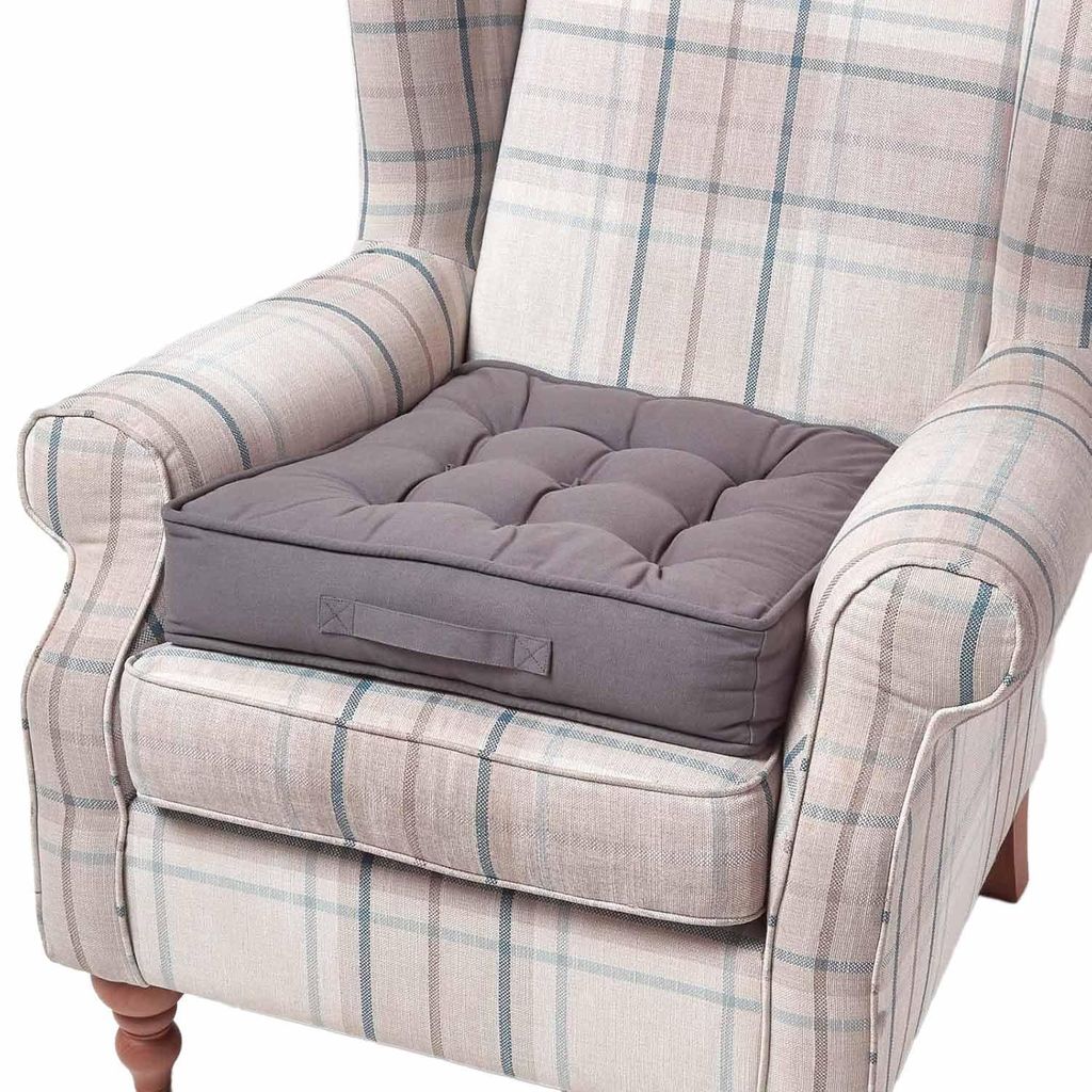 A grey cushion sits on a plaid armchair.